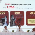 Stage with a large screen showing 'Target Penetapan CbPn Tahun 2026' and a target of 1,750; three red panels with cultural artifacts; three officials sit at a white-clothed table with microphones and small plants.
