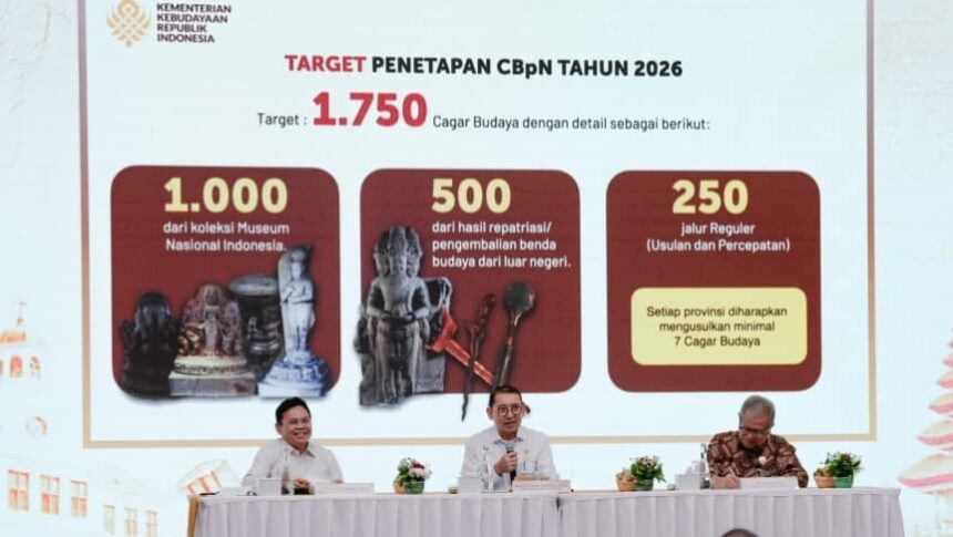 Stage with a large screen showing 'Target Penetapan CbPn Tahun 2026' and a target of 1,750; three red panels with cultural artifacts; three officials sit at a white-clothed table with microphones and small plants.
