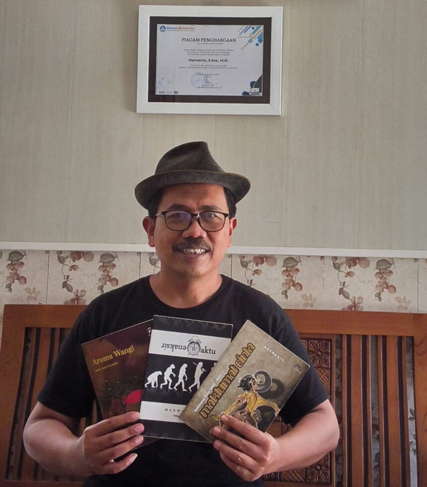 Smiling man wearing a hat and glasses sits on a wooden bench, holding three books in front of a framed certificate on the wall behind him.