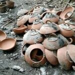 Pile of broken clay pots scattered on a sooty ground outdoors.