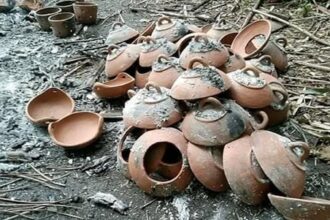 Pile of broken clay pots scattered on a sooty ground outdoors.