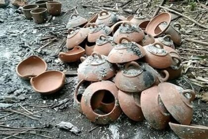 Pile of broken clay pots scattered on a sooty ground outdoors.