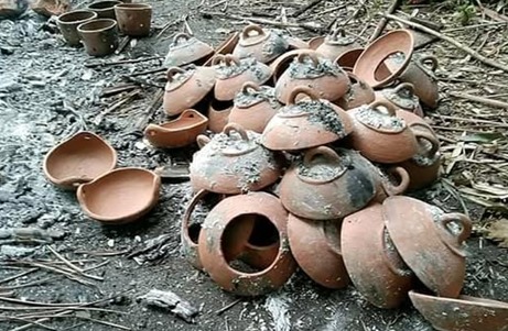 Pile of broken clay pots scattered on a sooty ground outdoors.