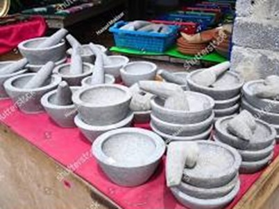 Collection of gray stone mortars and pestles of various sizes arranged on a pink cloth at a market stall.