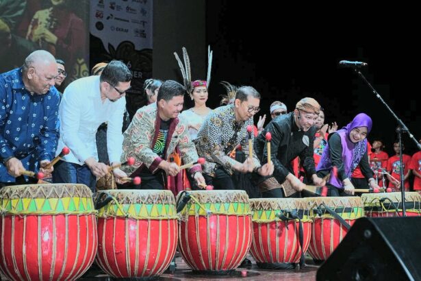 Group of diverse performers on stage playing large red and yellow drums with mallets during a cultural performance.