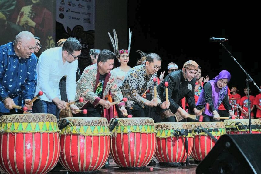 Group of diverse performers on stage playing large red and yellow drums with mallets during a cultural performance.