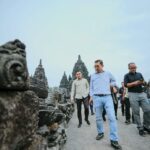 Group of men walking along ancient stone temple ruins on a wide pathway.