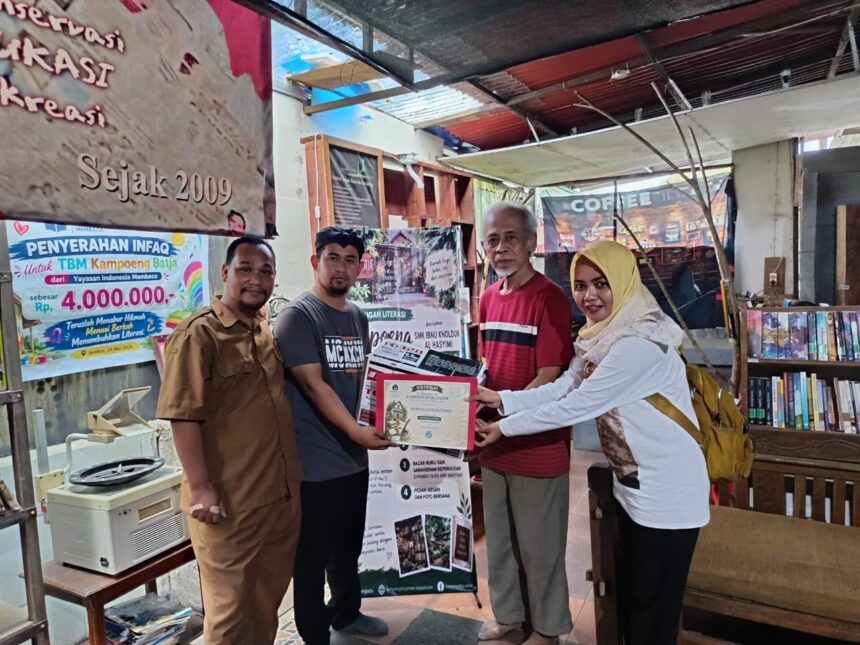 Group of four people posing as one person receives a certificate in a small library or bookshop setting, with banners and books in the background.