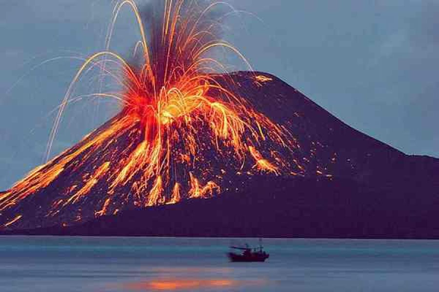 Active volcano erupting with lava jets flowing down its slopes, a dark hillside below, and a small boat on a calm body of water in the foreground.