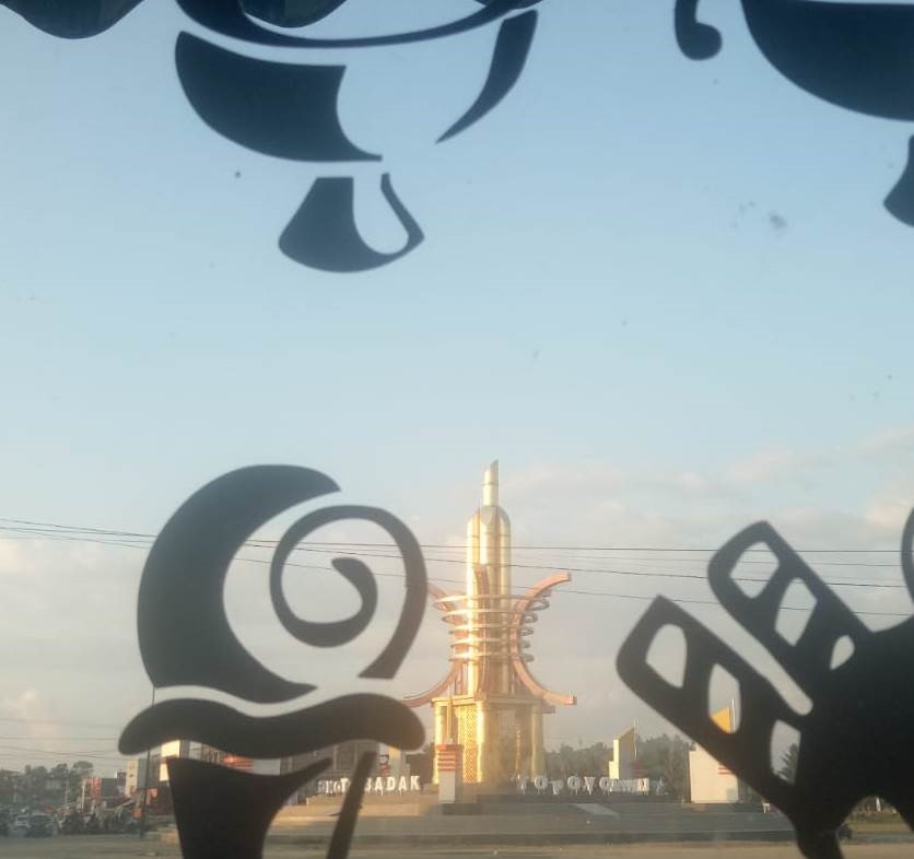 View through decorative window cutouts of a tall golden tower with curved fins in the distance, in a parking lot setting