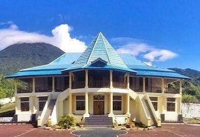 WhatsApp Image 2026-09-14 at 104137 - Mabur.co Two-story beige building with a turquoise roof and a central pyramid tower, set against a blue sky and mountains behind it.