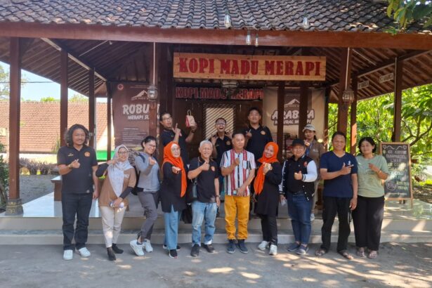 Group of people posing for a photo in front of a rustic coffee stall labeled 'Kopi Madu Merapi', outdoors on a sunny day.