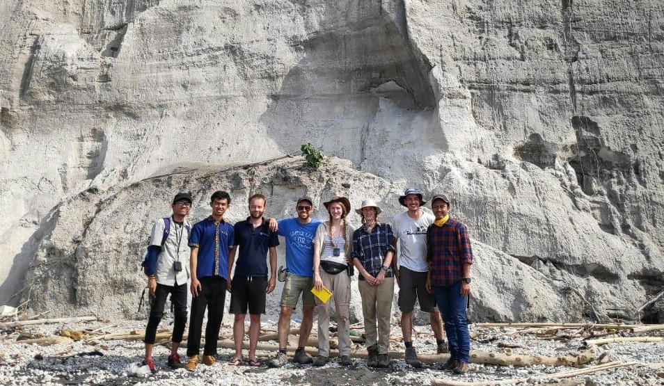 WhatsApp Image 2026-09-15 at 131342 - Mabur.co Group of nine people posing together on a pebbly beach with a white chalk cliff behind them, smiling for the photo.