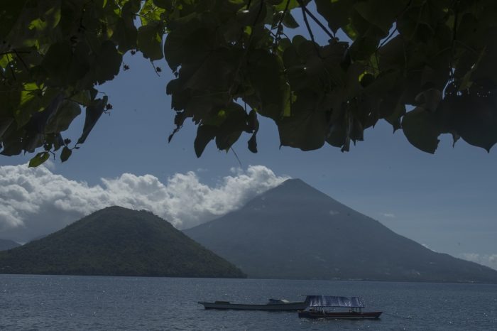 WhatsApp Image 2026-09-19 at 0810051 - Mabur.co Two volcanic islands rise from a blue lake under a clear sky, with a small boat anchored in the foreground.