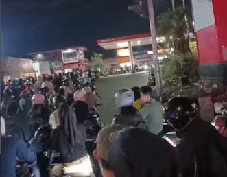 Crowd of people and motorcycles gathered outside a lit storefront at night.