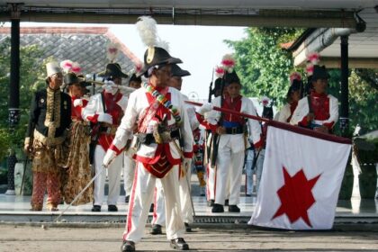 Historical reenactment: soldiers in white uniforms with plumed hats performing on a stage, carrying a white flag with a red star.