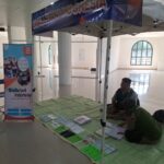 Informational booth for Braille Indonesia set up under a canopy in a bright hall, with banners, a folding chair, and brochures on a green mat for visitors with visual impairments.