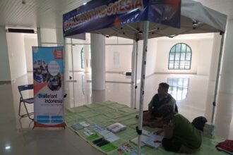 Informational booth for Braille Indonesia set up under a canopy in a bright hall, with banners, a folding chair, and brochures on a green mat for visitors with visual impairments.