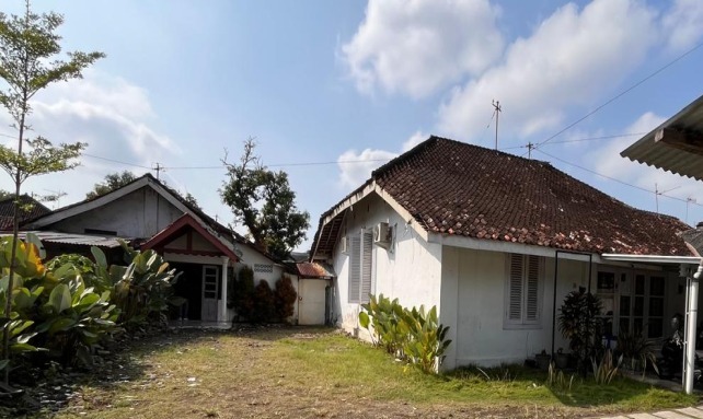 Two single-story white houses with red-tiled roofs in a fenced yard under a blue sky.