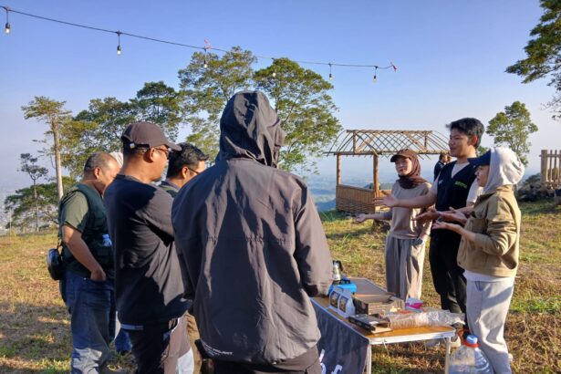 Group of people gathered around a table outdoors on a hillside, presenting or discussing items as a wooden cart backdrop sits nearby.