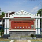 Entrance sign for Kalurahan Argomulyo in Yogyakarta with decorative columns and district crest, set among greenery and parked cars