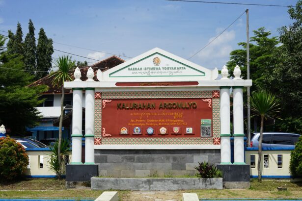 Entrance sign for Kalurahan Argomulyo in Yogyakarta with decorative columns and district crest, set among greenery and parked cars