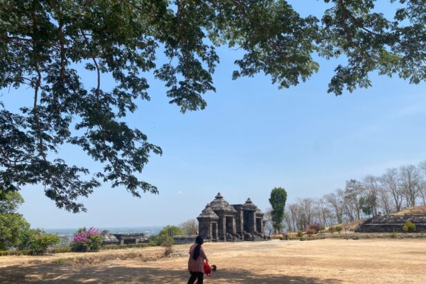 Stone temple ruin in an open park with a blue sky and trees framing the scene; a woman and child walk in the foreground.