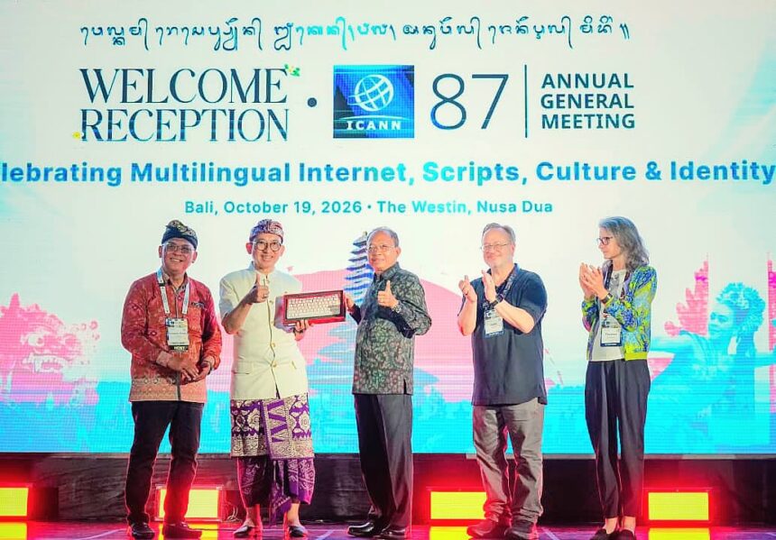 Five people on a stage clapping at the ICANN 87 Annual General Meeting welcome reception, with a bright screen displaying event text behind them and one person holding a plaque in the center.