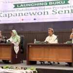 Four panelists sit at a conference table on a stage, microphones in front, with a large 'LAUNCHING BUKU' banner in the background.
