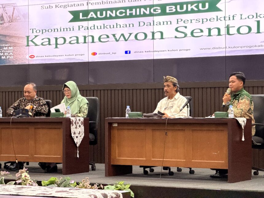 Four panelists sit at a conference table on a stage, microphones in front, with a large 'LAUNCHING BUKU' banner in the background.