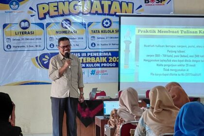 Man in beige shirt speaking into a handheld microphone on a stage, with a large 'PENGUATAN' banner and a projected slide beside him.