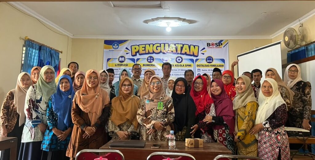 WhatsApp Image 2026-10-21 at 130212 - Mabur.co Group of men and women posing for a photo in a classroom, front row smiling, with a banner reading 'PENGUATAN' in the background.