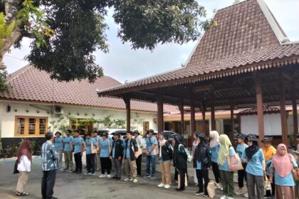 Group of people in blue shirts lined up in an outdoor courtyard, listening to an instructor at the front.