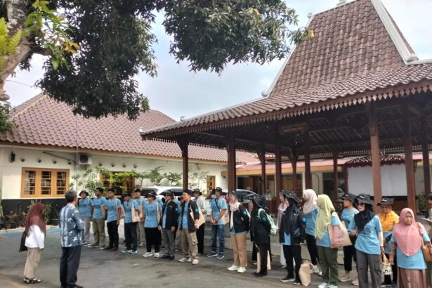 Group of people in blue shirts lined up in an outdoor courtyard, listening to an instructor at the front.