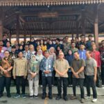 Large group of men and women posing for a group photo under a wooden pavilion outdoors.