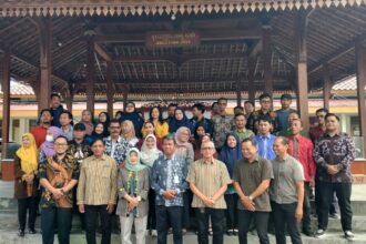 Large group of men and women posing for a group photo under a wooden pavilion outdoors.