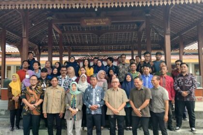 Large group of men and women posing for a group photo under a wooden pavilion outdoors.