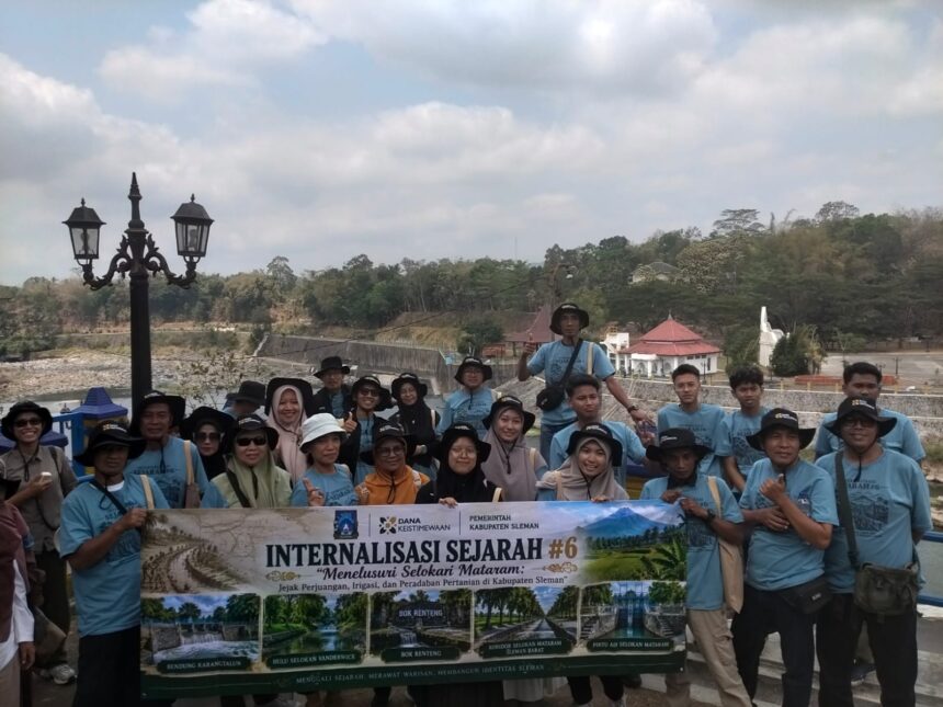 Group of tourists in matching light-blue shirts posing with a banner outdoors, with a decorative lamppost and hillside background.
