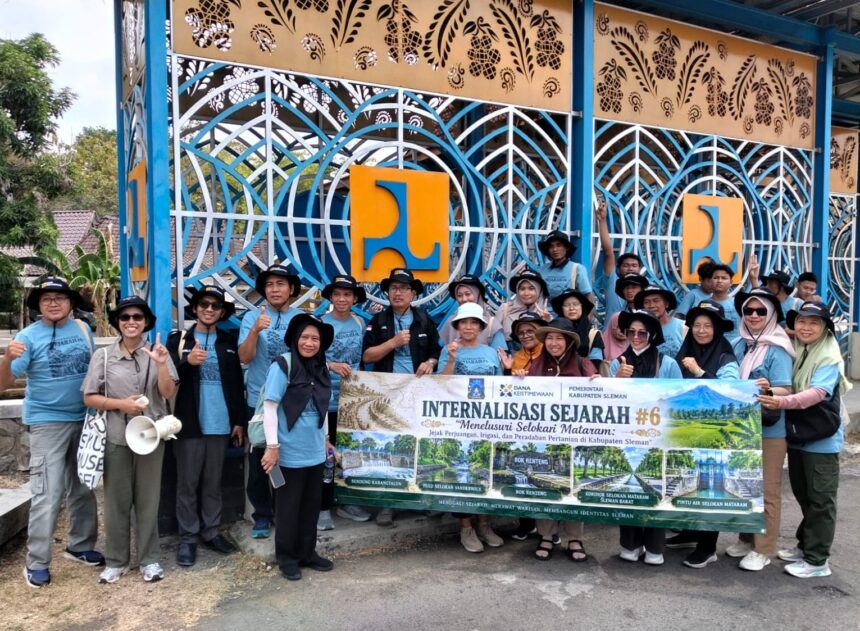 Group of people in blue shirts and hats pose with a large banner outdoors in front of an intricate blue gate backdrop.