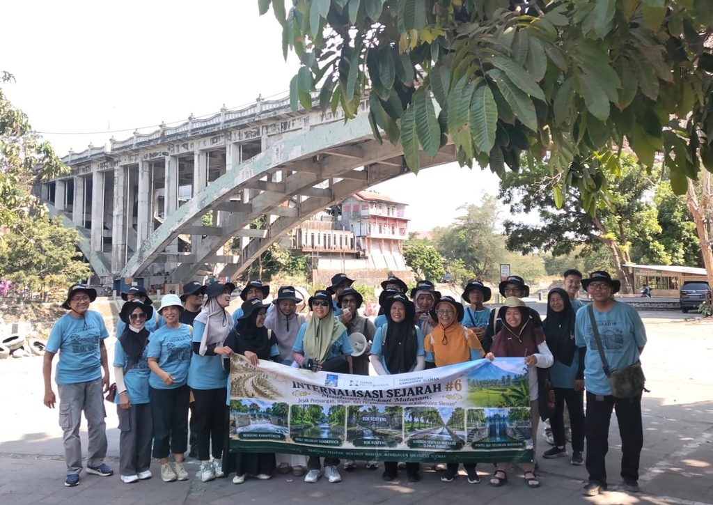 Group of people in blue shirts posing with a banner under a large concrete arch bridge.