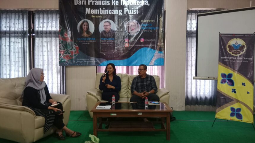 Panel discussion in a conference room with two people seated on a cream sofa and a woman on the left taking notes; a banner behind them advertises a poetry discussion event and logos are visible on the banner.
