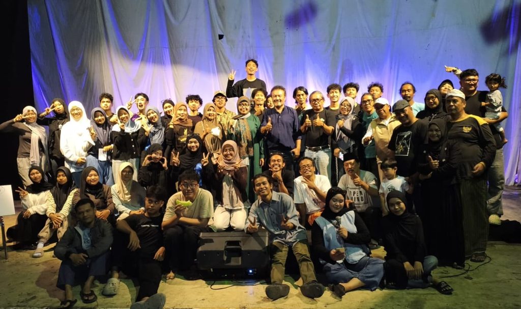 WhatsApp Image 2026-10-26 at 082219 - Mabur.co Large diverse group of people posing together on a stage, smiling and giving thumbs up after a performance event.