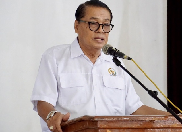 Man in a white short-sleeve shirt speaks at a wooden podium with a microphone in front of him.