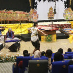 Traditional Indonesian dance performance on a decorated stage with gamelan musicians and two dancers in center, audience watching.