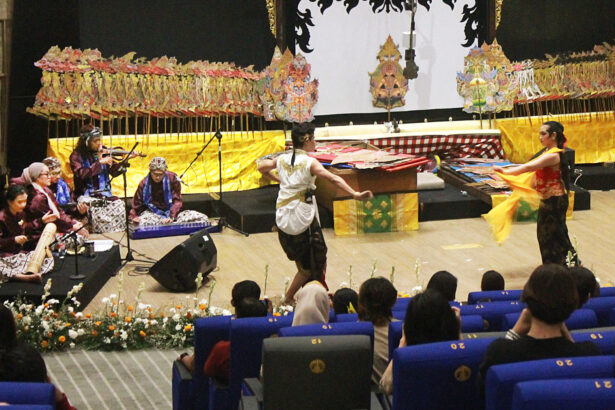 Traditional Indonesian dance performance on a decorated stage with gamelan musicians and two dancers in center, audience watching.