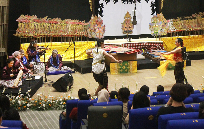 Traditional Indonesian dance performance on a decorated stage with gamelan musicians and two dancers in center, audience watching.