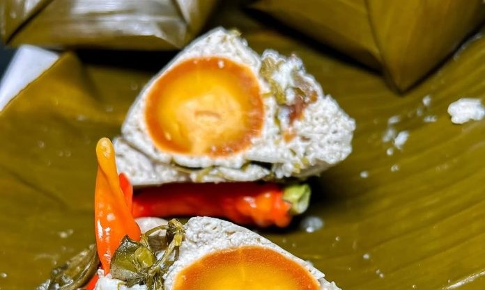 Two dim sum pieces with bright orange salted‑egg yolks inside a white crumbly exterior, garnished with carrot and green toppings on a banana leaf