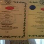 Two diplomas with green laurel borders are being held up by hands on each side, left featuring a gold seal and right a blue seal.