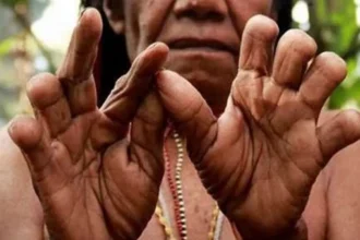 Close-up of dark-skinned hands forming a circle with thumbs and index fingers, beads visible in the background