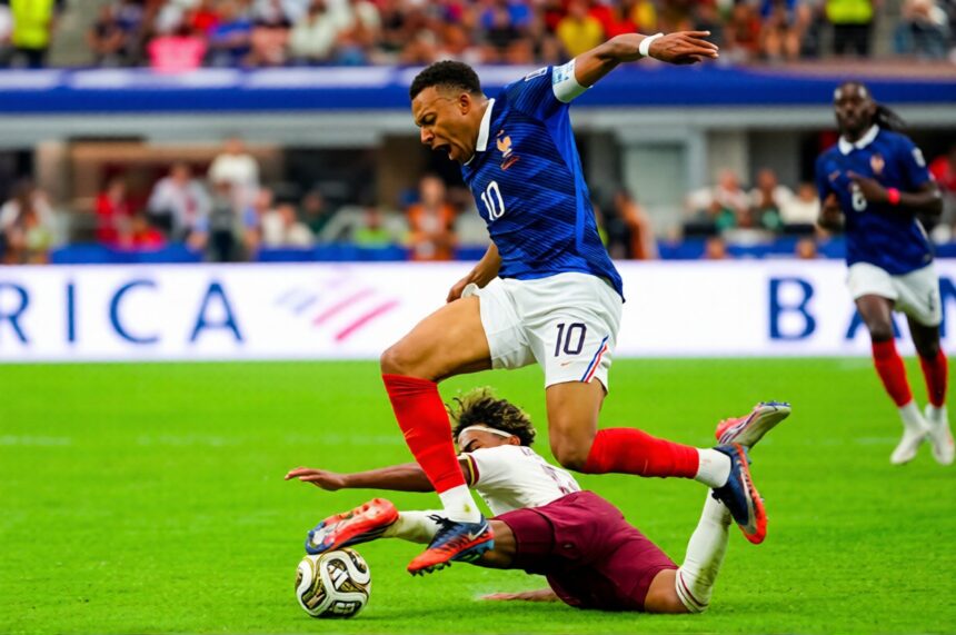 France footballer wearing blue jersey number 10 leaps over a sliding tackle toward the ball on a green pitch.